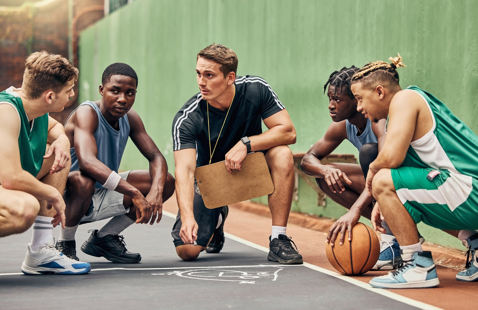 A basketball coach discusses X's and O's during a team huddle on the court.
