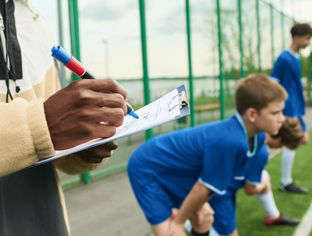male-coach-writing-notes-while-teenage-boys-warmin-2026-01-09-12-09-31-utc